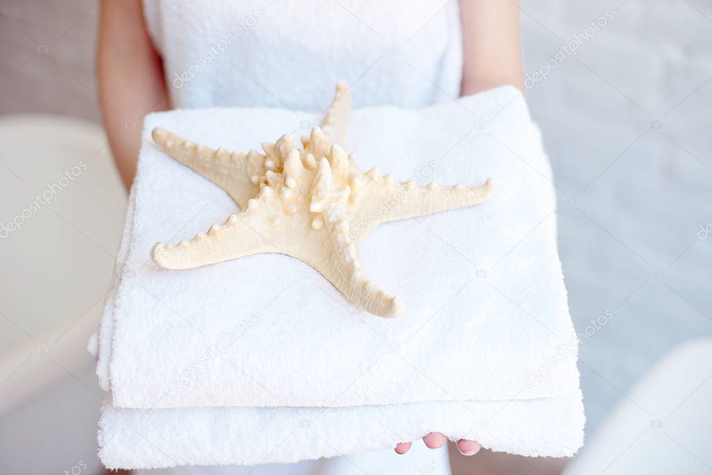 Close-up woman holding white bath towels decorated with starfish. Concept of Spa, Hotels, Resorts.