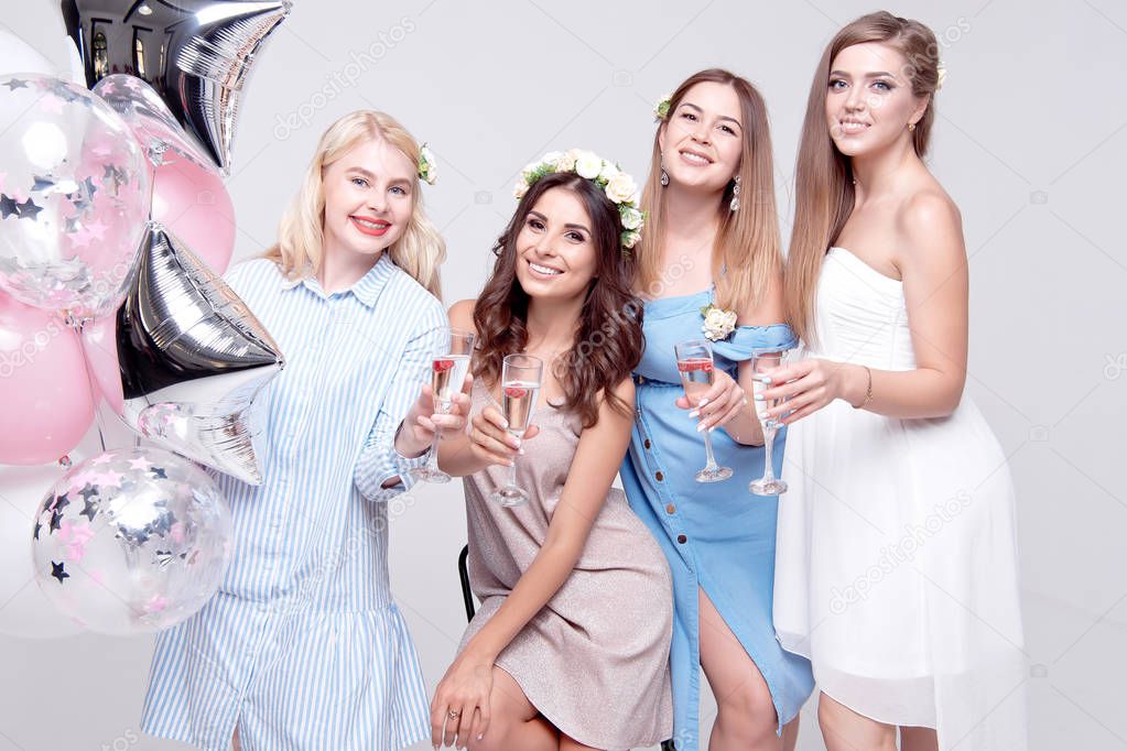happy girlfriends holding glasses with alcohol and balloons while celebrating bachelorette party.