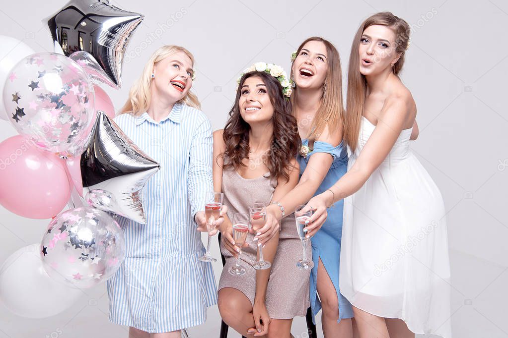 happy girlfriends holding glasses with alcohol and balloons while celebrating bachelorette party.