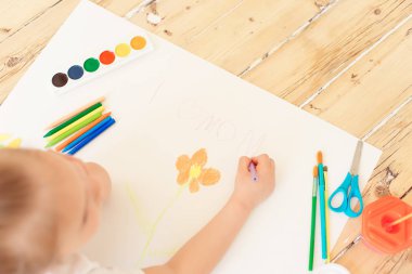 Küçük sarışın kız boyama çiçek beyaz kağıda üstten görünüm 