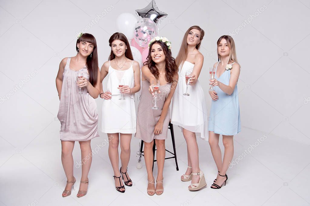 Smiling girlfriends holding glasses with champagne and having fun while celebrating bachelorette party isolated on white background