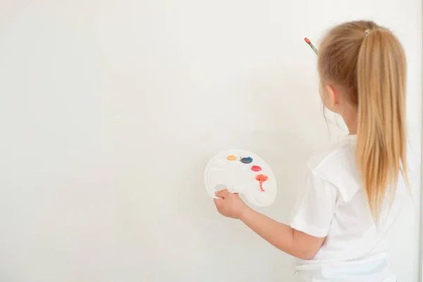 Cute little girl painting on wall in empty room — Stock Photo, Image