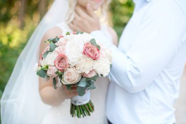 Close-up wedding couple standing side by side holding bouquets of flowers in white-pink colors. clipart