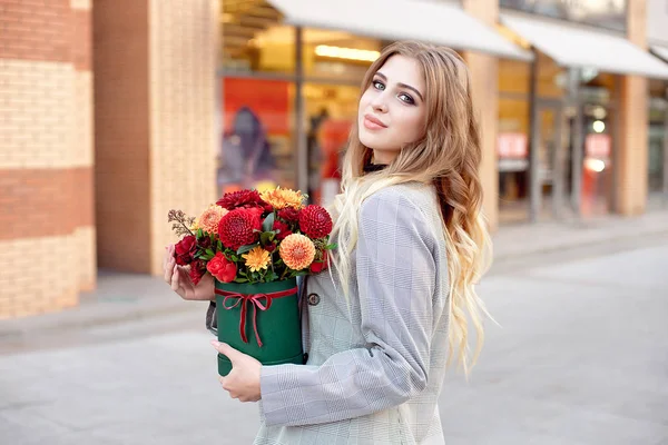 幸せな笑顔の花箱を持って店頭店の窓近くの路上に立っている白人ファッション女性 — ストック写真