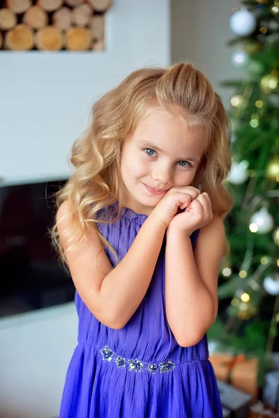 Feliz niña en vestido de lujo púrpura toma de las manos cerca de face.With luces de colores y el árbol de Navidad en el fondo. Vacaciones, Navidad, año nuevo, x-mas concep —  Fotos de Stock