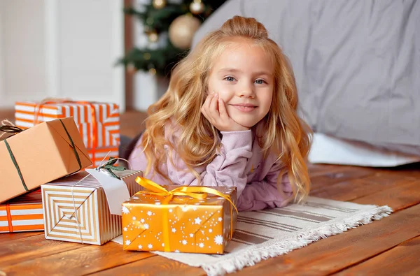 Arka plan Christmas tree yatakta yakın yerdeki yalan kıvırcık saçlı sarışın saçlı güzel küçük kız. Noel hediyesi.