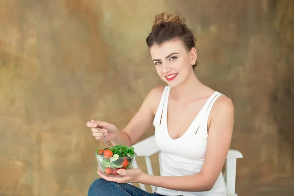 Чудова здорова жінка сидить на білому стільці, їсть здоровий салат з рук, органічні помідори . — стокове фото