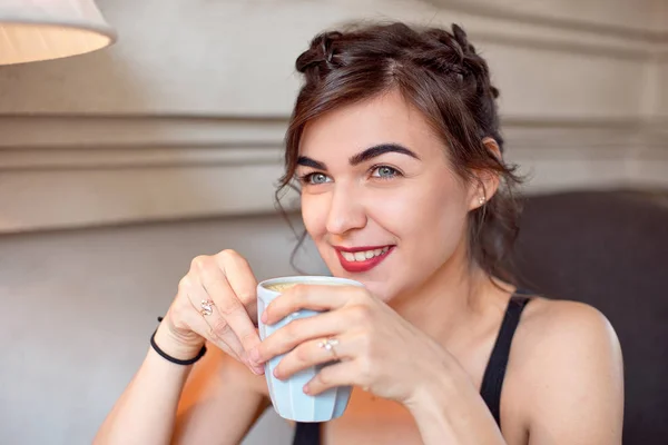 Junges attraktives Mädchen in schwarzem T-Shirt und Jeans sitzt in einem Café am Tisch und trinkt Kaffee in einer Vintage-Tasse. — Stockfoto