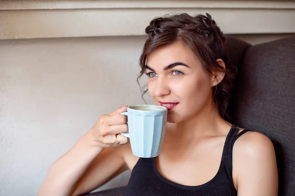 Junges attraktives Mädchen in schwarzem T-Shirt und Jeans sitzt in einem Café am Tisch und trinkt Kaffee in einer Vintage-Tasse. — Stockfoto