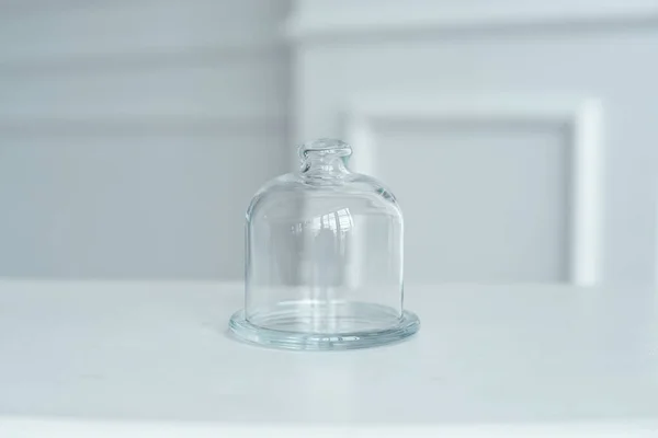 The glass cap for the cake stand is on a white table in a bright room.