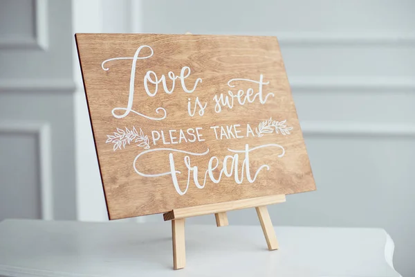 The close-up photo of the wooden plaque with the signs Love to the wedding standing on white background