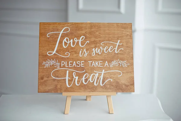 The close-up photo of the wooden plaque with the signs Love to the wedding standing on white background