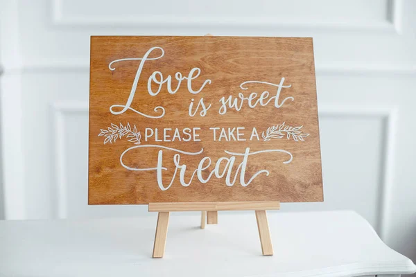 The close-up photo of the wooden plaque with the signs Love to the wedding standing on white background