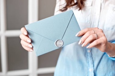 Mavi dikdörtgen hediye zarf ile davetiye, mal ve hizmet kartı tutan bir genç kızın yakın çekim.