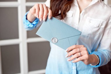 Mavi dikdörtgen hediye zarf ile davetiye, mal ve hizmet kartı tutan bir genç kızın yakın çekim.