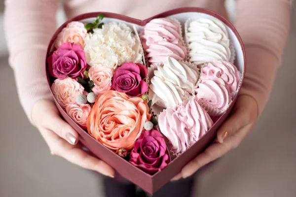 A bouquet of flowers and marshmallows in a gift box of heart in female hands. Congratulatory concept, sale. — Stock Photo, Image