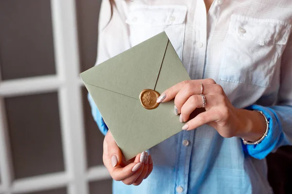 Gros plan femme avec un corps mince tenant dans les mains la carte d'invitation couleur gris-vert forme carrée enveloppe carte . — Photo