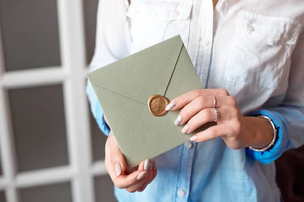 Close-up mulher com corpo magro segurando nas mãos o cartão de convite cor cinza-verde cartão de envelope forma quadrada . — Fotografia de Stock