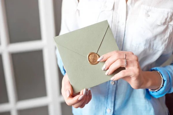 Mujer de cerca con cuerpo delgado sosteniendo en las manos la tarjeta de invitación tarjeta de sobre de forma cuadrada de color gris-verde . —  Fotos de Stock