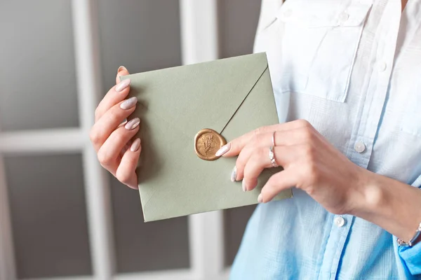 Close-up mulher com corpo magro segurando nas mãos o cartão de convite cor cinza-verde cartão de envelope forma quadrada . — Fotografia de Stock