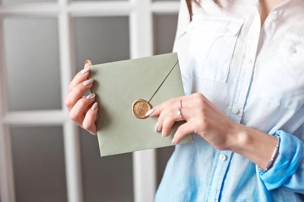 Mujer de cerca con cuerpo delgado sosteniendo en las manos la tarjeta de invitación tarjeta de sobre de forma cuadrada de color gris-verde . —  Fotos de Stock