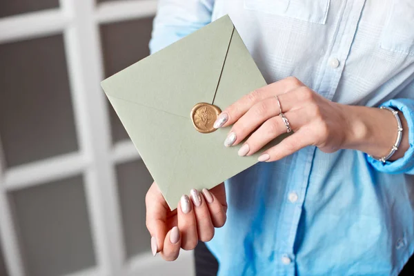 Mujer de cerca con cuerpo delgado sosteniendo en las manos la tarjeta de invitación tarjeta de sobre de forma cuadrada de color gris-verde . —  Fotos de Stock