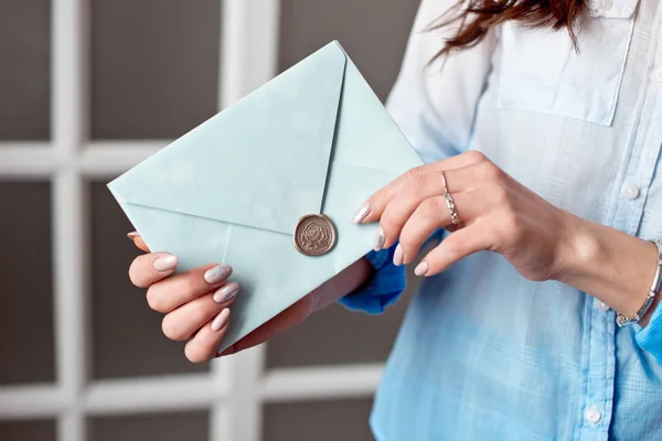 Nahaufnahme einer Frau mit schlankem Körper, die eine blaue, rechteckige Einladungskarte im Umschlag einer Karte hält. — Stockfoto