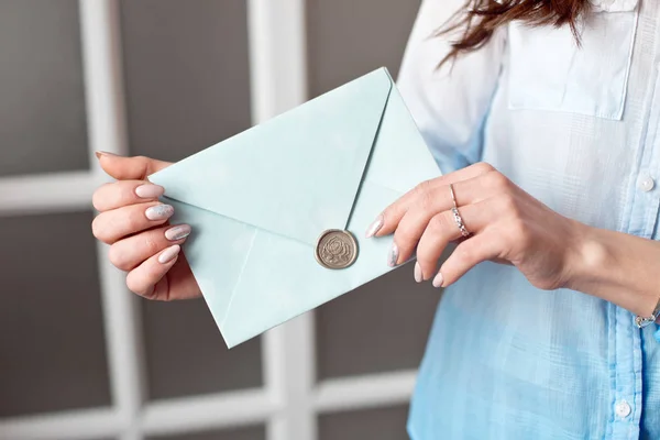 Nahaufnahme einer Frau mit schlankem Körper, die eine blaue, rechteckige Einladungskarte im Umschlag einer Karte hält. — Stockfoto