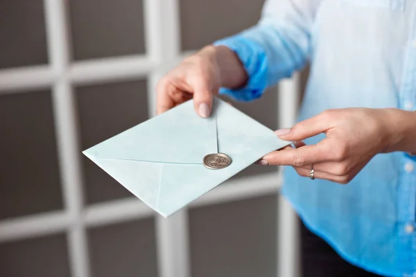 Närbild av en kvinna med en smal kropp håller en blå rektangulär inbjudan kort i ett kuvert med ett kort. — Stockfoto