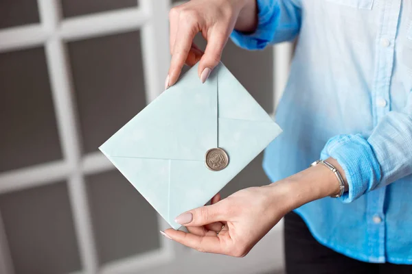 Närbild av en kvinna med en smal kropp håller en blå rektangulär inbjudan kort i ett kuvert med ett kort. — Stockfoto