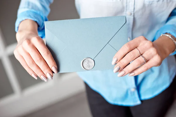 Close-up de uma jovem segurando um envelope de presente retangular azul com convites, bens e serviços cartão . — Fotografia de Stock