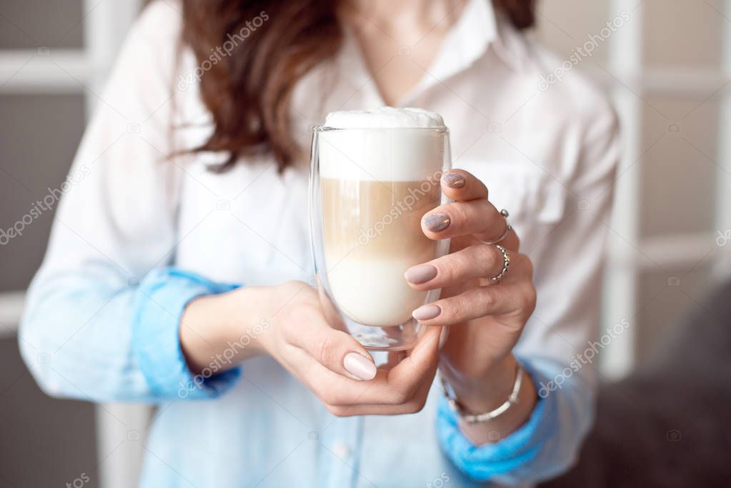 Close-up of female hands in office clothes holding a glass cup of coffee with soy milk during a break at work, lifestyle concept.