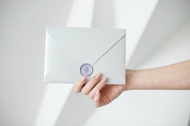 Bir mum mühür, hediye çeki, kartpostal, düğün davetiye kartı ile gümüş davetiye zarf tutan eller, yakın çekim fotoğraf.