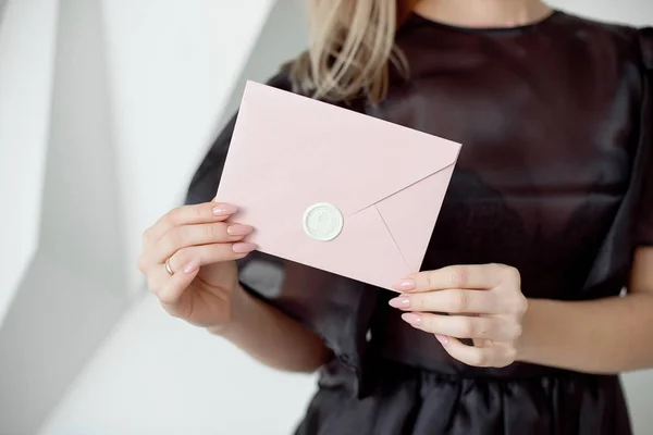 Foto de close-up de uma mão feminina segurando um envelope de convite rosa com um selo de cera, um certificado de presente, um cartão, um cartão de convite de casamento . — Fotografia de Stock