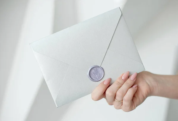 Foto de close-up de mãos femininas segurando um envelope de convite de prata com um selo de cera, um certificado de presente, um cartão postal, um cartão de convite de casamento . — Fotografia de Stock