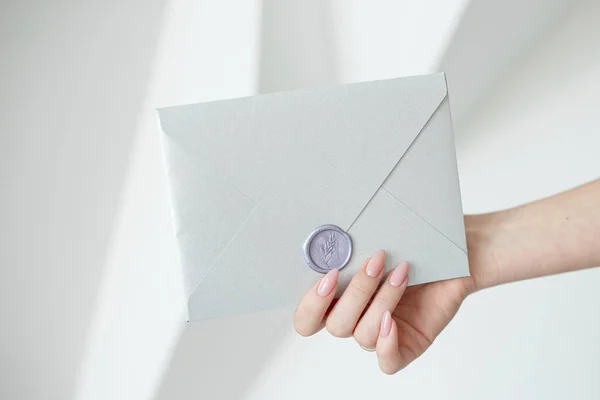 Nahaufnahme von weiblichen Händen mit einem silbernen Einladungsumschlag mit Wachssiegel, einem Gutschein, einer Postkarte, einer Hochzeitseinladungskarte. — Stockfoto