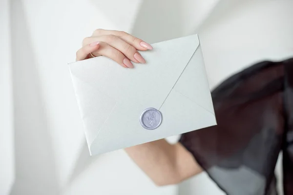 Foto de close-up de mãos femininas segurando um envelope de convite de prata com um selo de cera, um certificado de presente, um cartão postal, um cartão de convite de casamento . — Fotografia de Stock