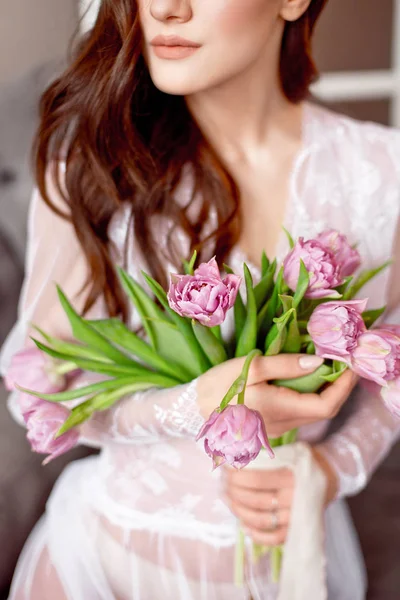 自宅のベッドの上の花チューリップと白いドレスの美しい若い女性の手します — ストック写真