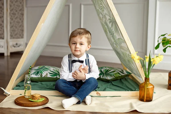 Un bambino in abiti da vacanza è seduto in una tenda nella sua stanza — Foto Stock