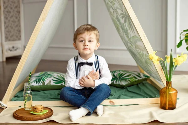 Un bambino in abiti da vacanza è seduto in una tenda nella sua stanza — Foto Stock
