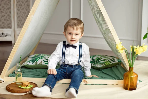 Un bambino in abiti da vacanza è seduto in una tenda nella sua stanza — Foto Stock