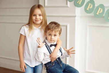 Beyaz gömlekli sevimli çocuk oturuyor parlak bir odada bir sandalyeye kardeş omuzlarını hugs