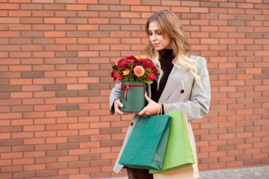 Çiçek-box mutlu gülümseme ile tutarak vitrin vitrinler yakınında sokakta duran beyaz moda kadın.