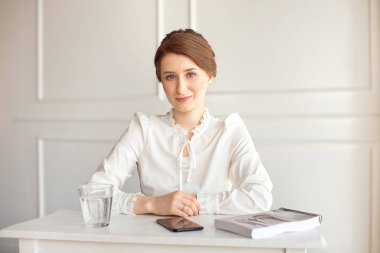 Parlak modern bir iş istasyonunda kağıtlarla çalışan beyaz bir gömlek güzel gülümseyen genç esmer işkadını portre.