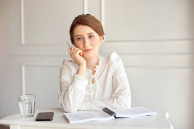 Parlak modern bir iş istasyonunda kağıtlarla çalışan beyaz bir gömlek güzel gülümseyen genç esmer işkadını portre.