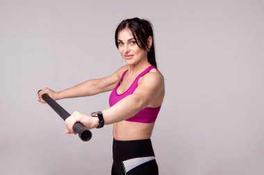 Güzel kaslı kadın gri bir arka plan üzerinde jimnastik sopa ile egzersiz yapıyor.