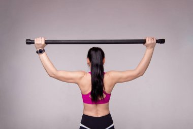 Güzel kaslı kadın gri bir arka plan üzerinde jimnastik sopa ile egzersiz yapıyor.