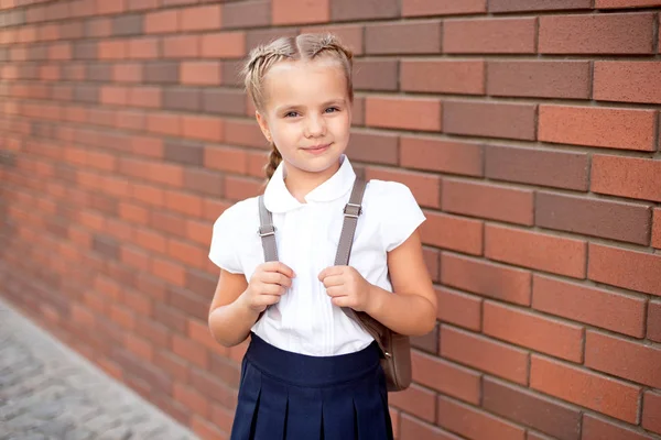 Bambina con i capelli biondi in camicia bianca e gonna blu tiene una tavola vuota vicino alla parete superiore — Foto Stock