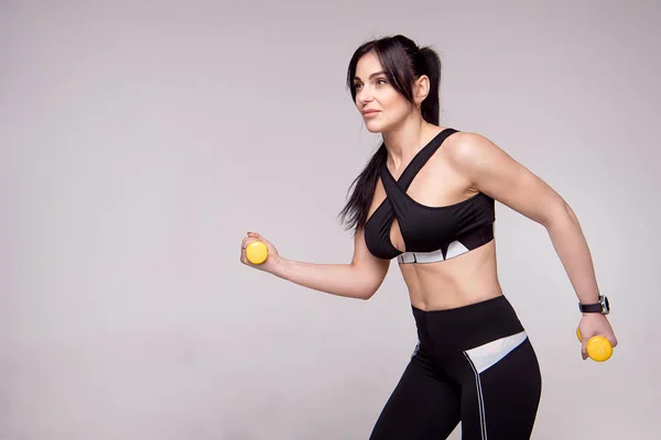 Retrato de una joven deportista europea haciendo ejercicios con pesas aisladas sobre fondo gris . — Foto de Stock