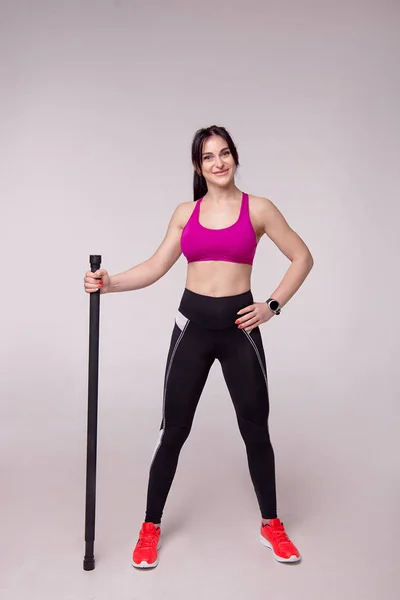 Hermosa mujer muscular haciendo ejercicio con palo de gimnasia sobre un fondo gris . — Foto de Stock